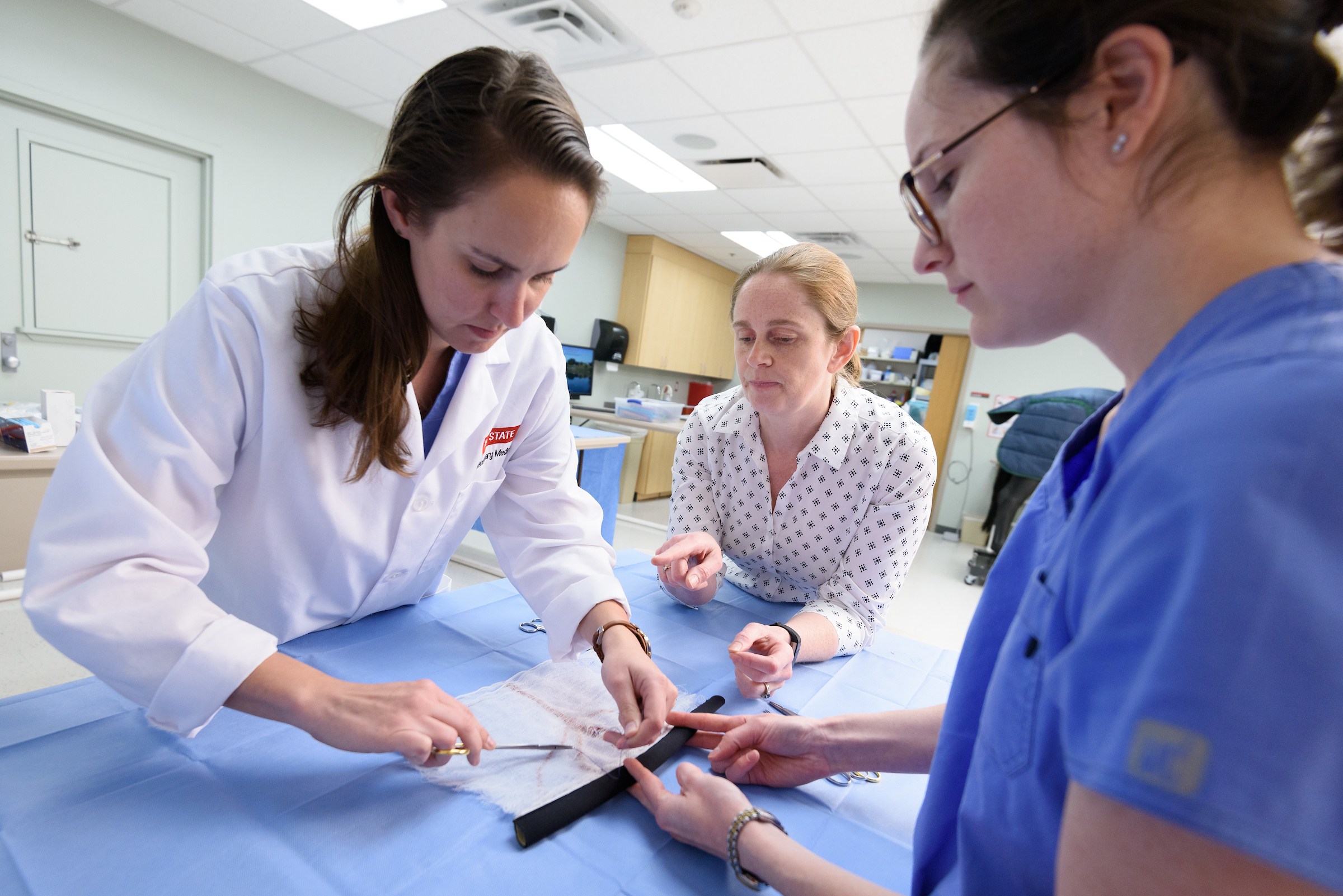 Three female doctors perform an anastamosis in a simulation lab.
