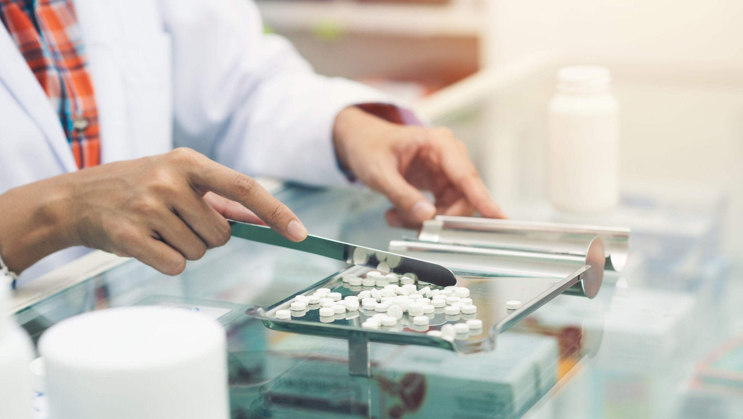 A pharmacist wearing a white coat counts pills on a metal tray.