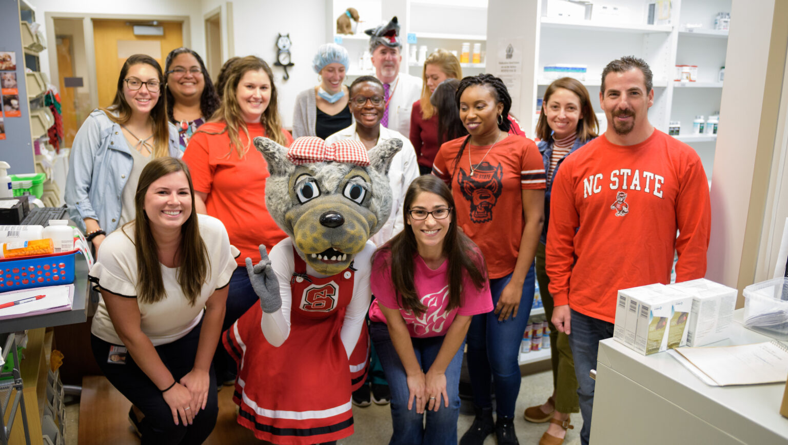 A group of students pose with Ms. Wuf, a person in an NC State mascot wolf costume.