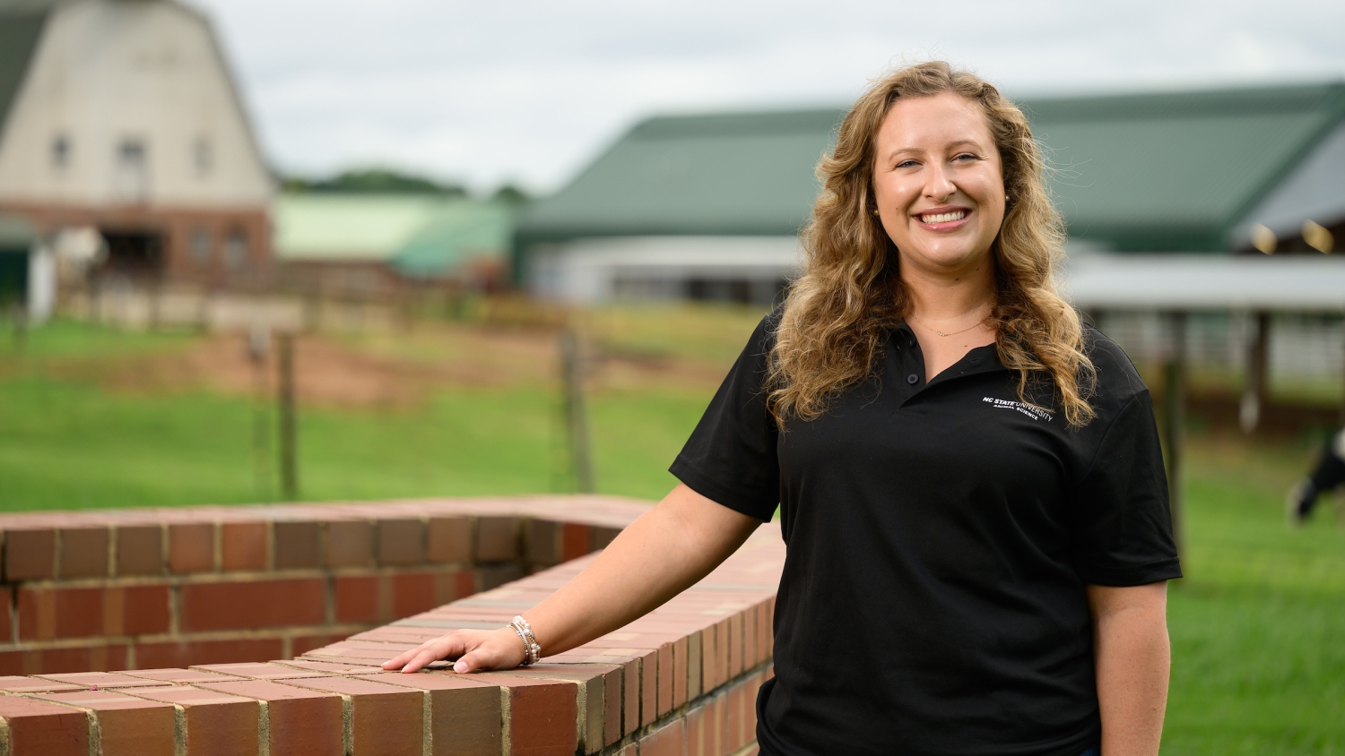 Lindsey Britton, a first-year student at the NC State College of Veterinary Medicine, stands in front of the Teaching Animal Unit barns outside the NC State CVM.